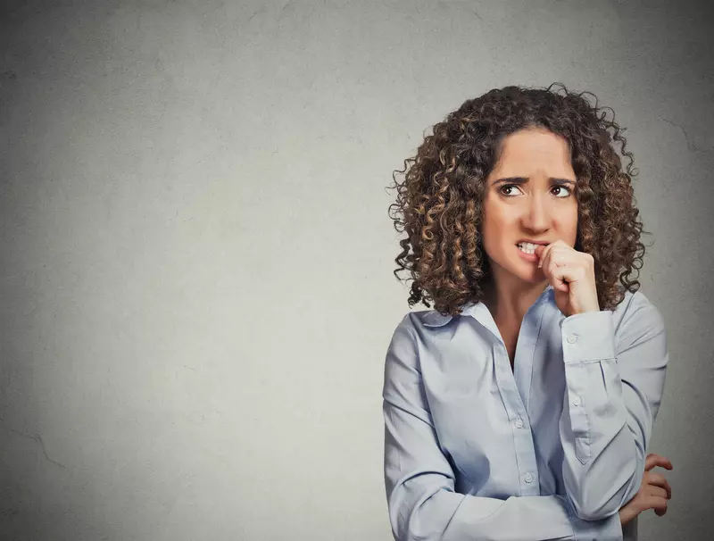 Woman biting her thumb nail and making a worried face while looking upwards
