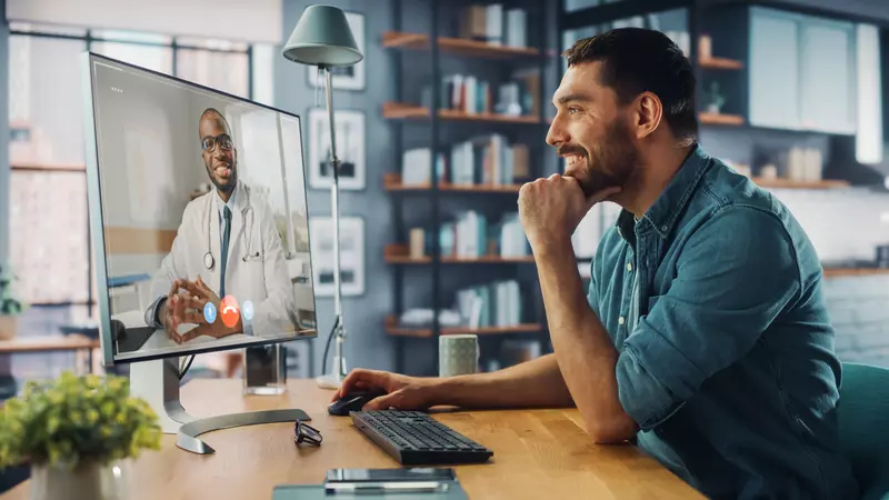 Man smiling at computer while talking with his doctor on the computer screen
